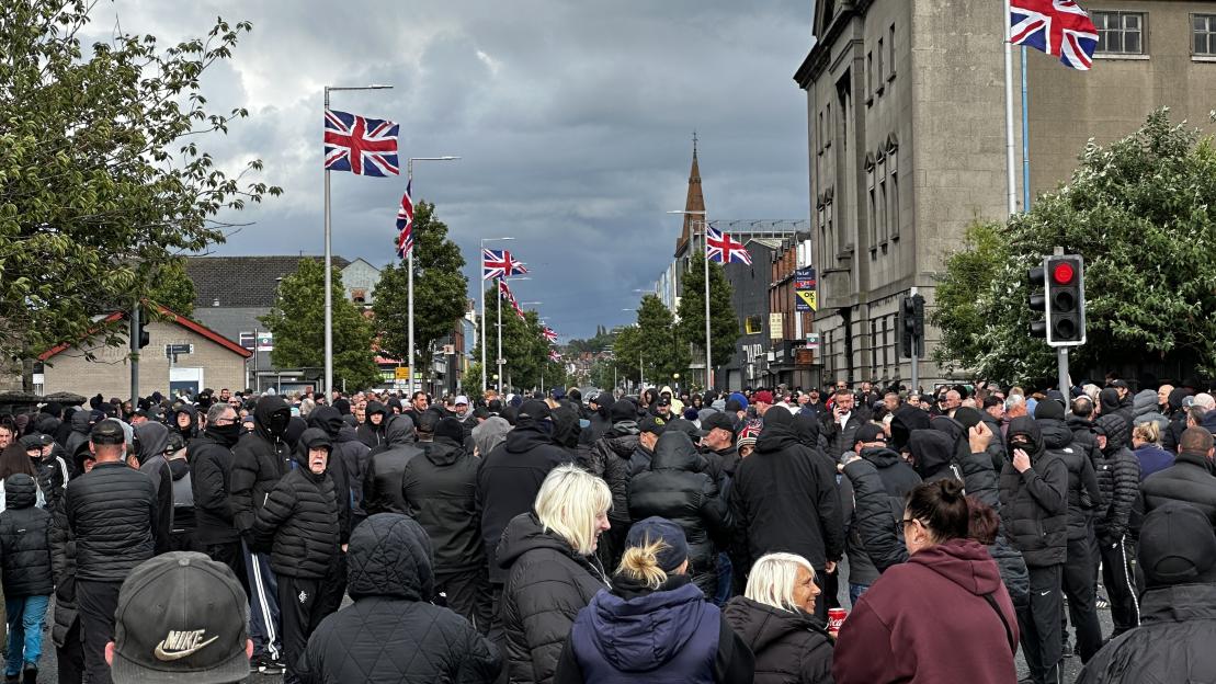 Protesters block Newtownards Road in East Belfast, with Union Jack flags lining the street.