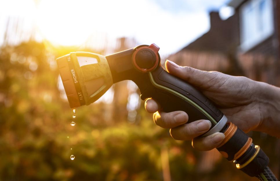 A person's hand holds a hosepipe with water dripping from its nozzle.