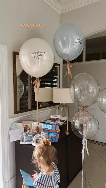 A young child looking at a card on a table with gifts and balloons.