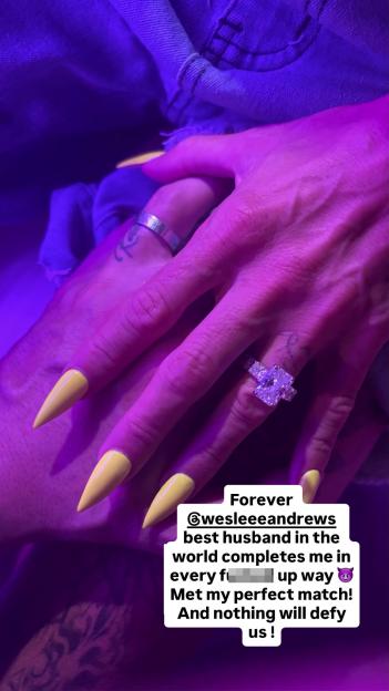 Close-up of Katie Price's left hand with yellow stiletto nails and a large engagement ring, holding another hand.