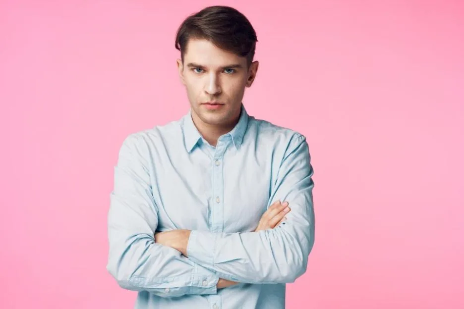 An offended man with crossed arms against a pink background.