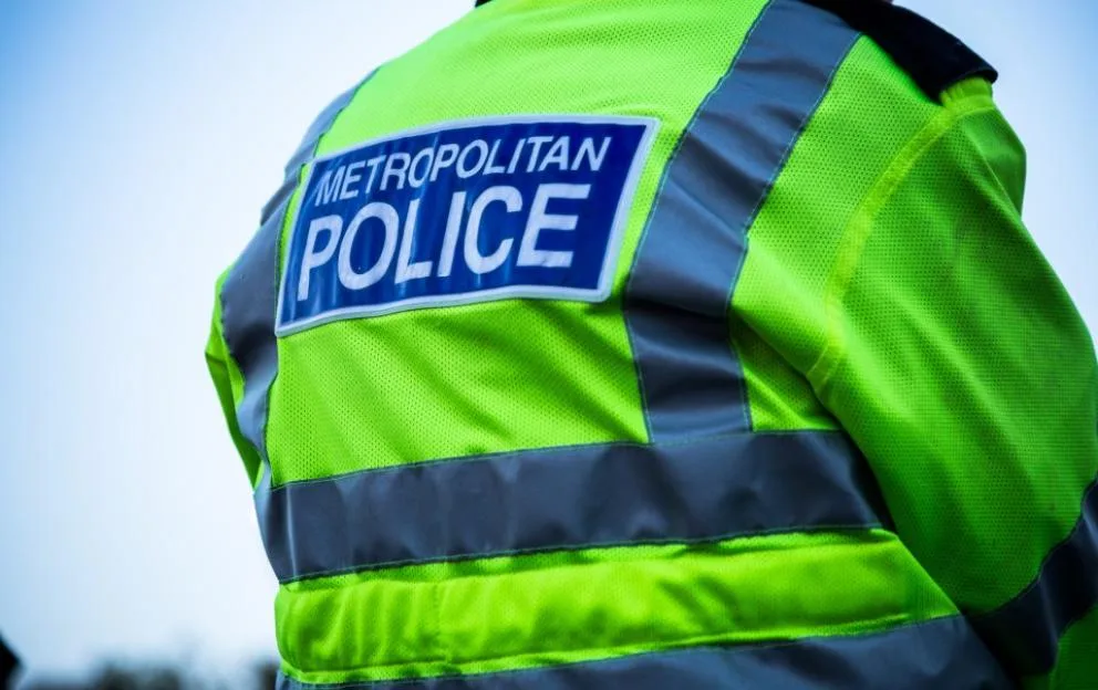 Back of a Metropolitan Police officer's uniform, showing a neon yellow jacket with reflective stripes and a blue patch reading "METROPOLITAN POLICE."