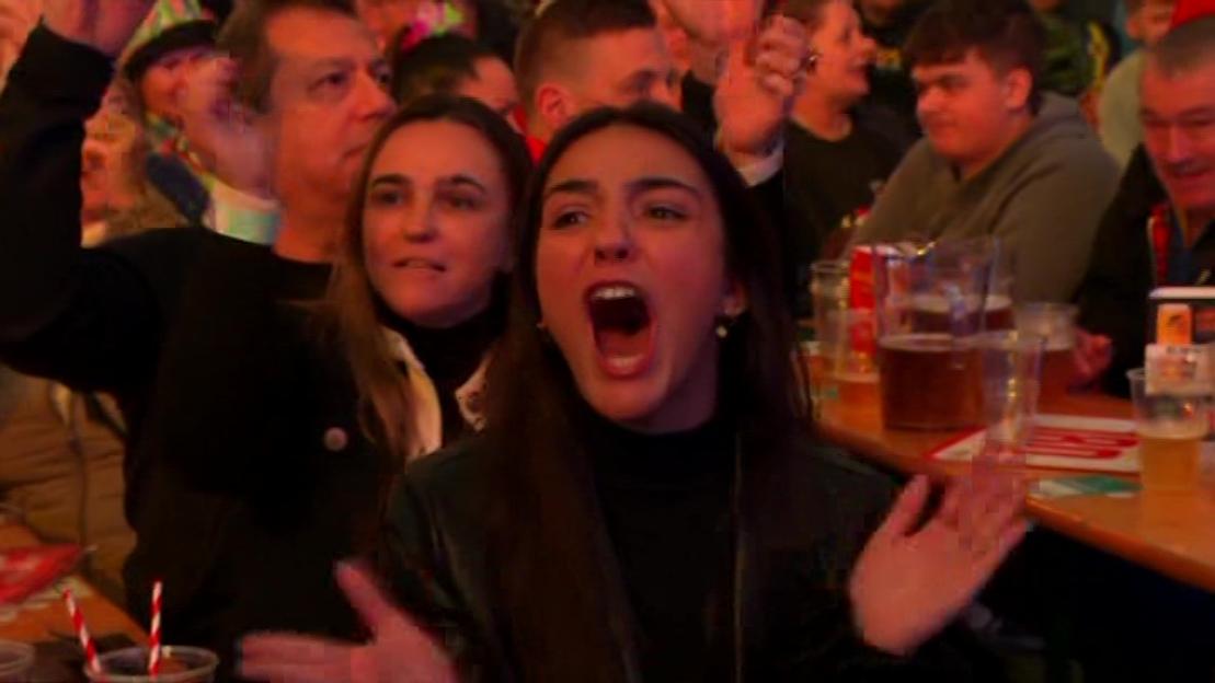 A crowd of people, including a woman with her mouth wide open, cheering in a bar.