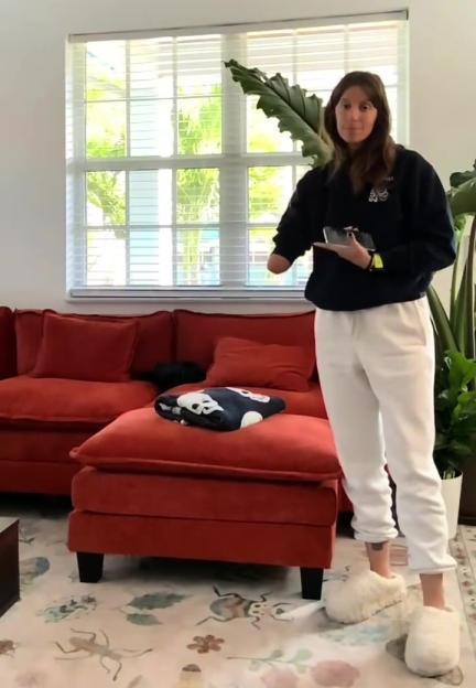 Woman holding a phone in her right hand, with her left arm ending above the elbow, standing in a living room.