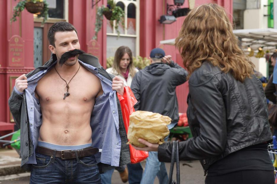 Ryan Malloy in a fake mustache and open shirt laughs with Janine Butcher.