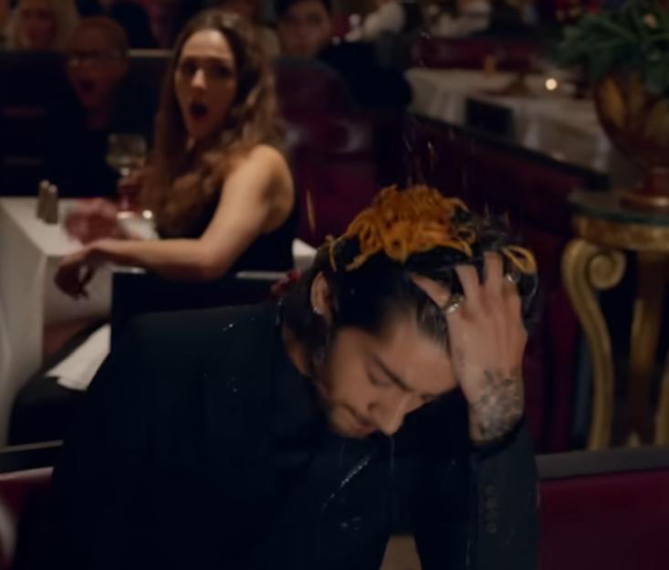 Man with spaghetti on his head in a restaurant, a woman looks on in shock.
