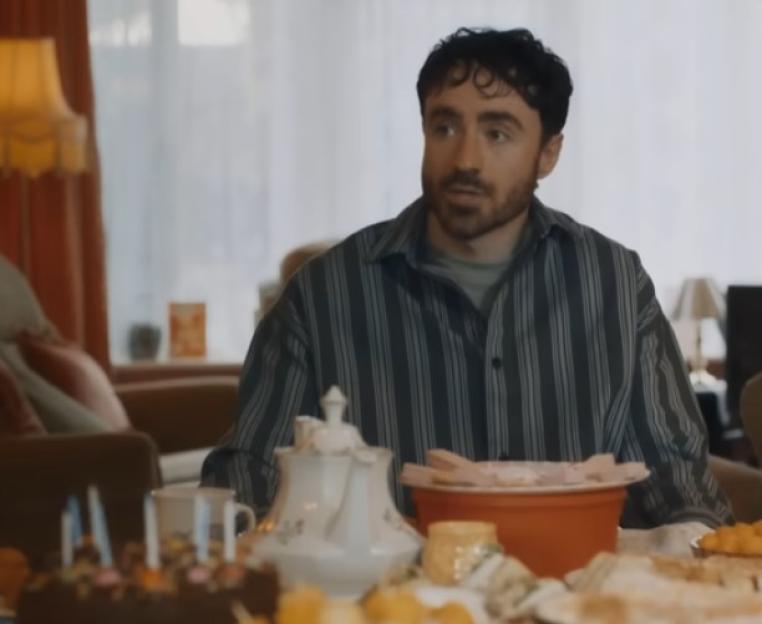 Man with dark hair and beard sitting at a table with a birthday cake.