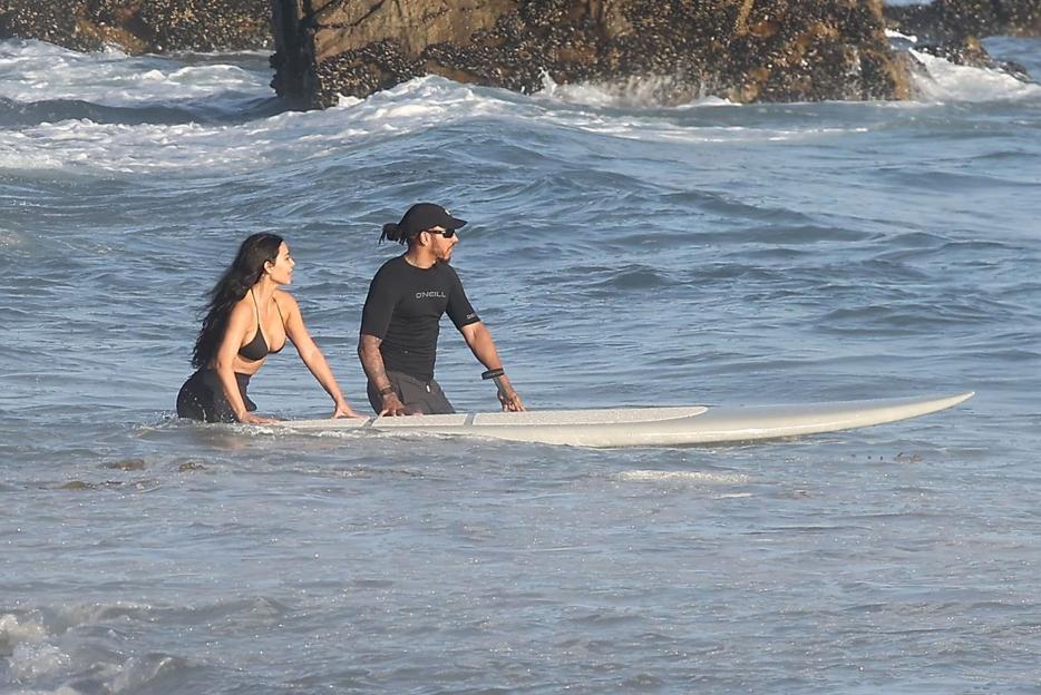 Kim Kardashian and Lewis Hamilton with a surfboard in the water.