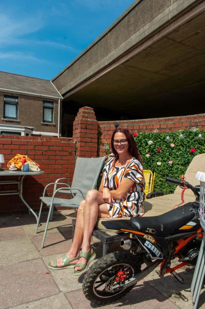 Kirsty Bowd sits in her backyard patio next to a mini dirt bike, with the M4 motorway overhead.