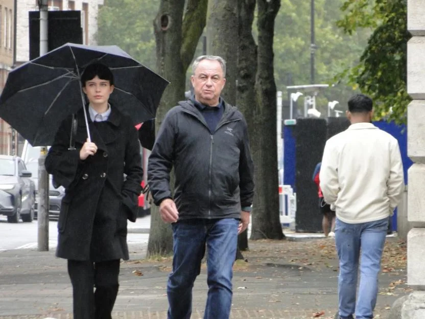 Aimee Gillingwater and Peter Gillingwater walk down a sidewalk, with Aimee holding an umbrella.