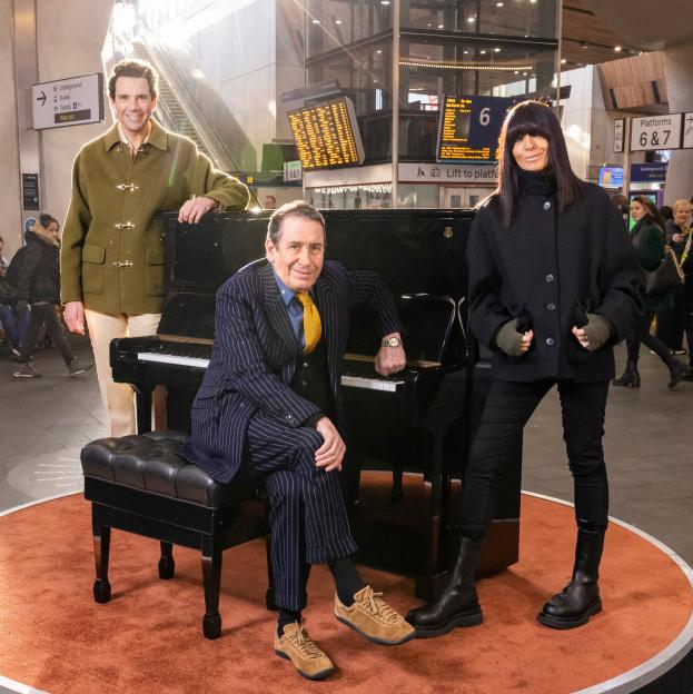 Mika, Andrew Lloyd Webber, and Claudia Winkleman posing with a piano at a train station.