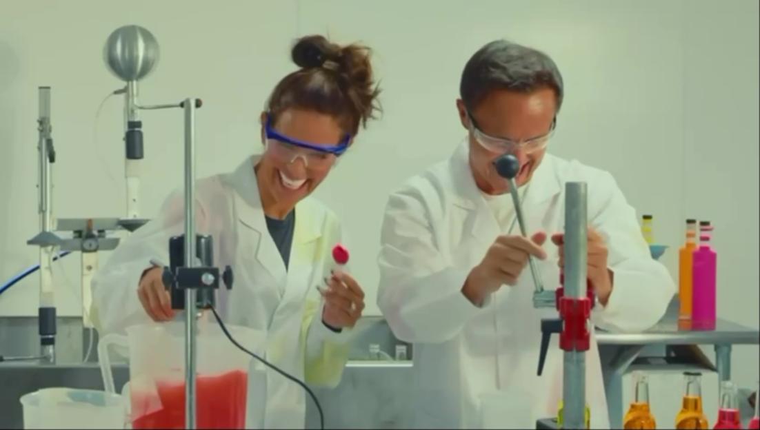 Becky Vardy and Dennis Wise laughing while mixing colorful liquids in a laboratory.