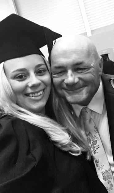 Becky Williams smiling in her graduation cap and gown next to a man in a suit and floral tie.
