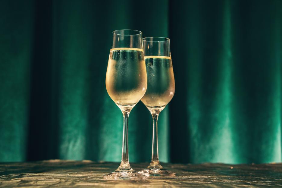 Two sweating champagne flutes on a table with a green curtain in the background.