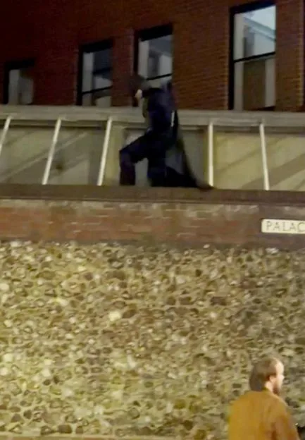A person dressed as Batman scales a building wall at night.