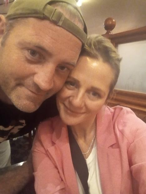 A man in a cap and a woman in a pink jacket posing closely for a selfie.