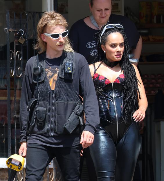 Charlie Cooper with a mullet and mustache, wearing a tactical vest, and Karla Crome with long braids, wearing a black latex outfit.