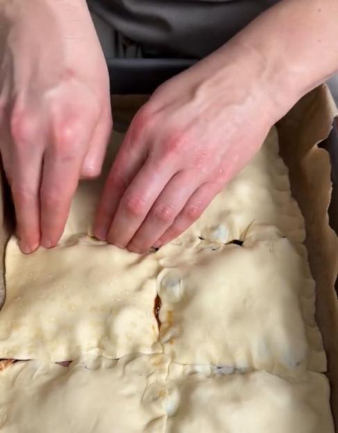 Two hands pressing together dough squares in a baking pan.