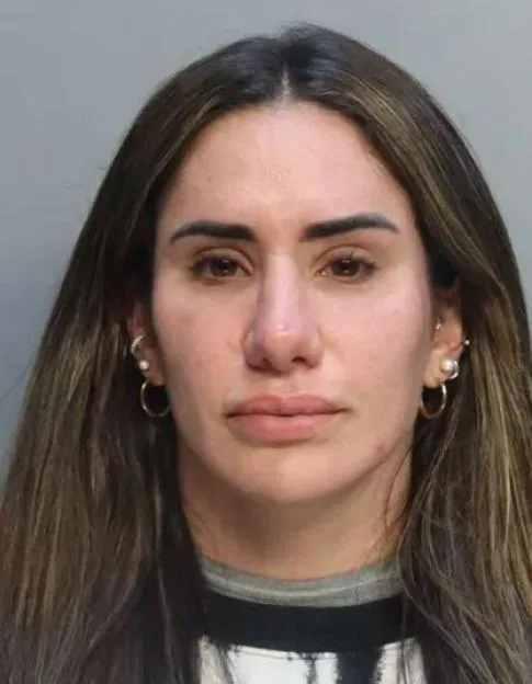 Mugshot of a woman with long dark hair, wearing earrings and a dark-rimmed shirt.