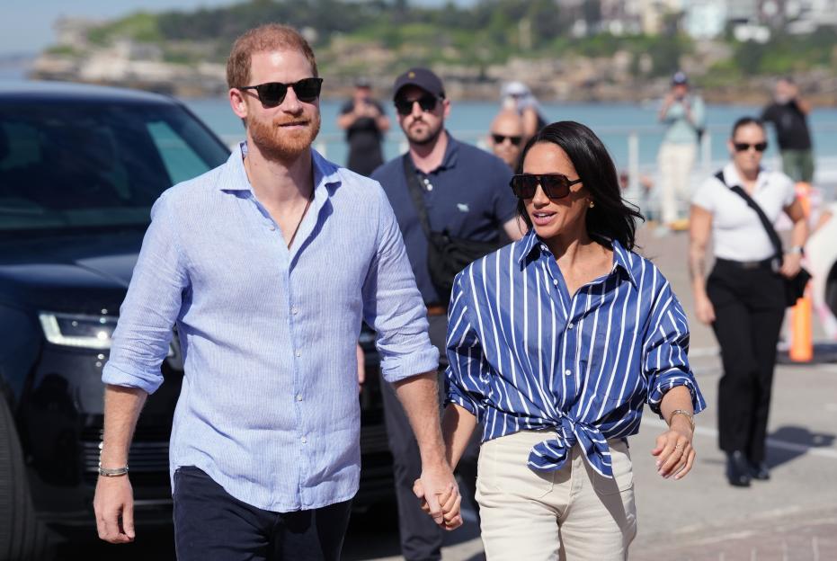 Prince Harry and Meghan, Duke and Duchess of Sussex, holding hands while arriving at an event in Bondi Beach, Australia.