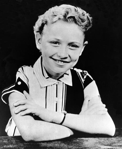 Black and white portrait of young Dolly Parton smiling with arms crossed.