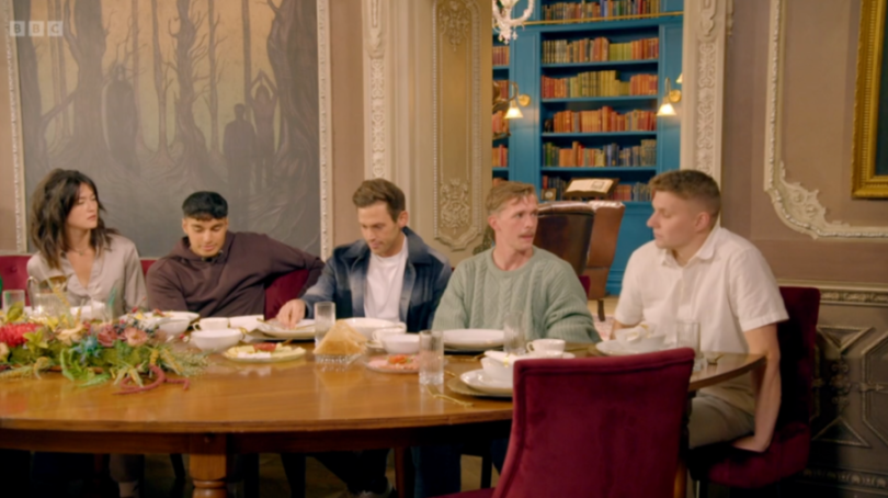 Reece from The Traitors sits at a dining table with four other contestants, two men and two women.