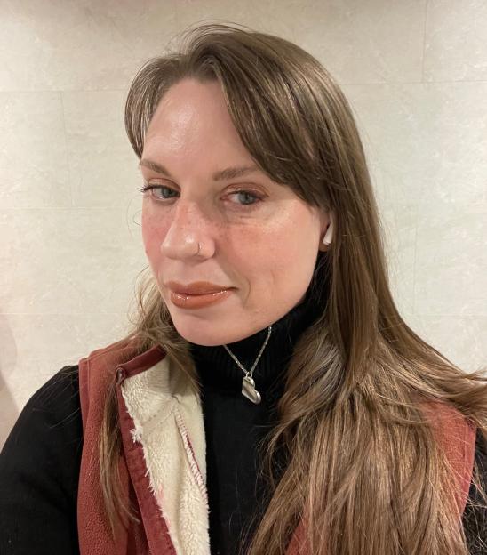 A woman with long brown hair, a nose ring, and a heart pendant necklace.