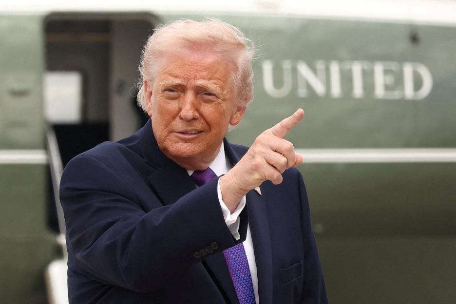 President Donald Trump gestures to the right, in front of a plane with "UNITED" visible.