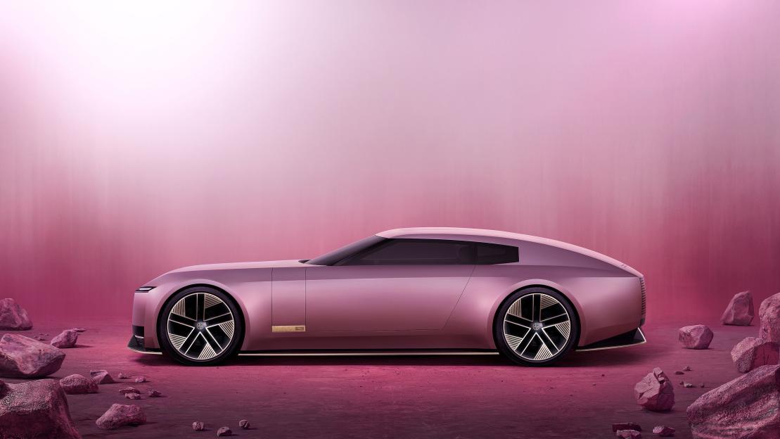 A pink Jaguar Type 00 concept car with a long hood and fastback profile, with 23-inch alloy wheels, surrounded by pink rocks.