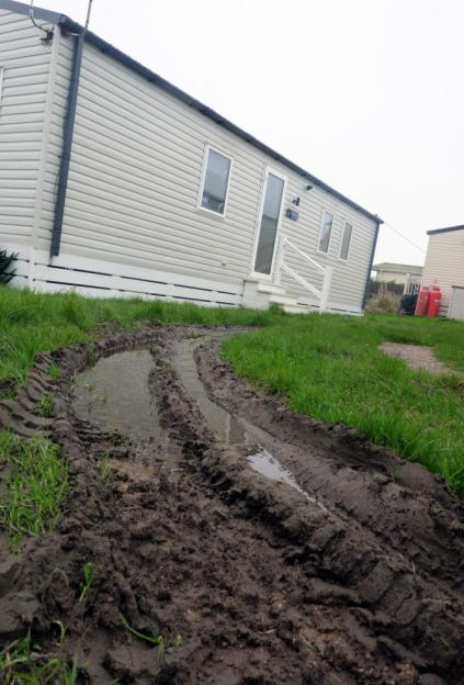 Tractor tire tracks filled with puddles in the muddy grass in front of a mobile home.