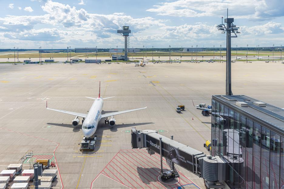 A Turkish Airlines plane parked at Berlin-Brandenburg Airport next to a jet bridge with "Revolut" branding.