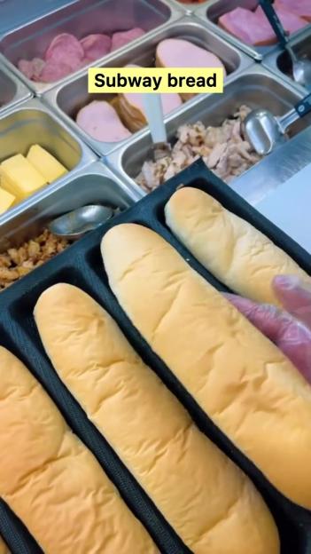 Subway bread rolls in a tray, next to containers of meat and cheese.