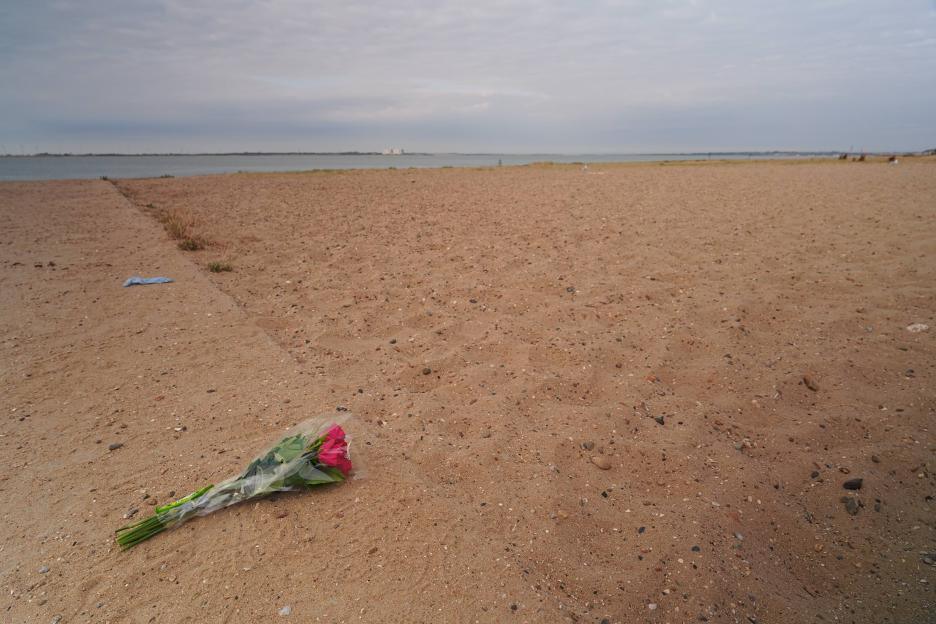 A bouquet of pink flowers wrapped in plastic lies on a sandy beach.