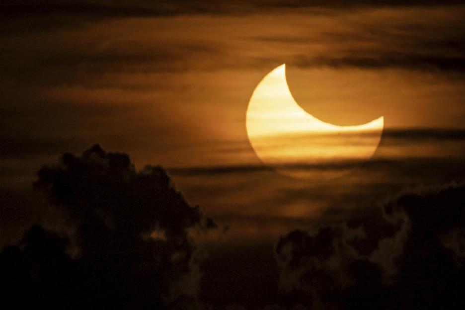 Partial solar eclipse at sunrise, with the moon covering the upper right quarter of the sun.