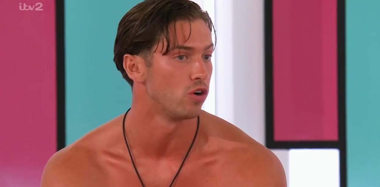 A man with dark hair and a tan is speaking, shown from the chest up.