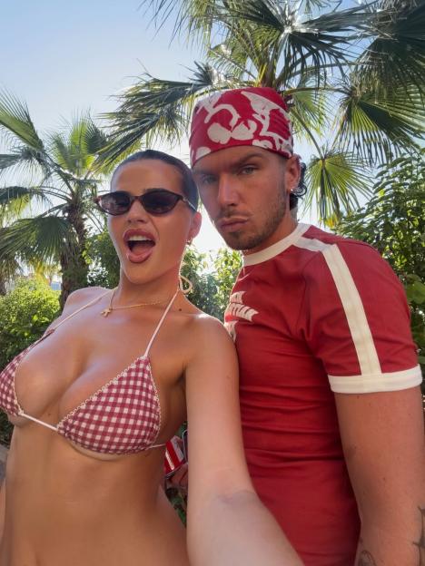 Matilda Draper and a man pose together outdoors under palm trees.
