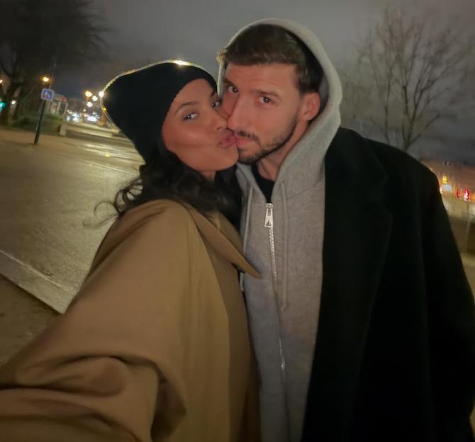 Maya Jama kissing Ruben Dias on the cheek, with a blurred street and lights in the background.