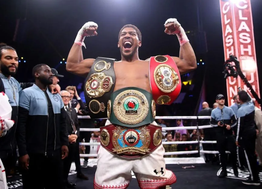 Anthony Joshua celebrates in the ring wearing his championship belts after defeating Andy Ruiz.