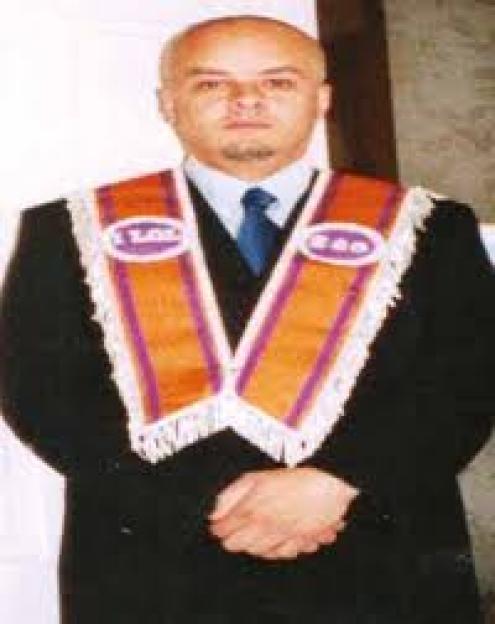 Nigel Bromage in a suit and an orange and purple sash with white fringe.