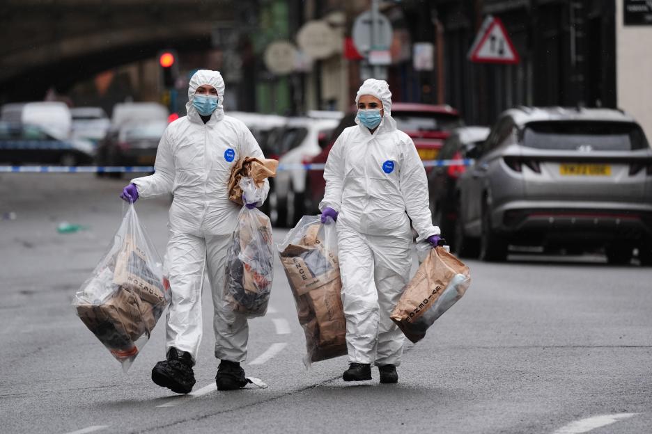 Forensic investigators in white suits and masks carrying evidence bags at a crime scene.