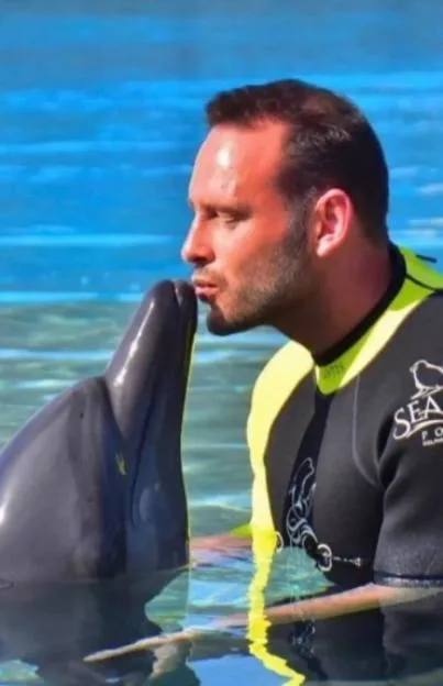 Lee Andrews kissing a dolphin in a pool.