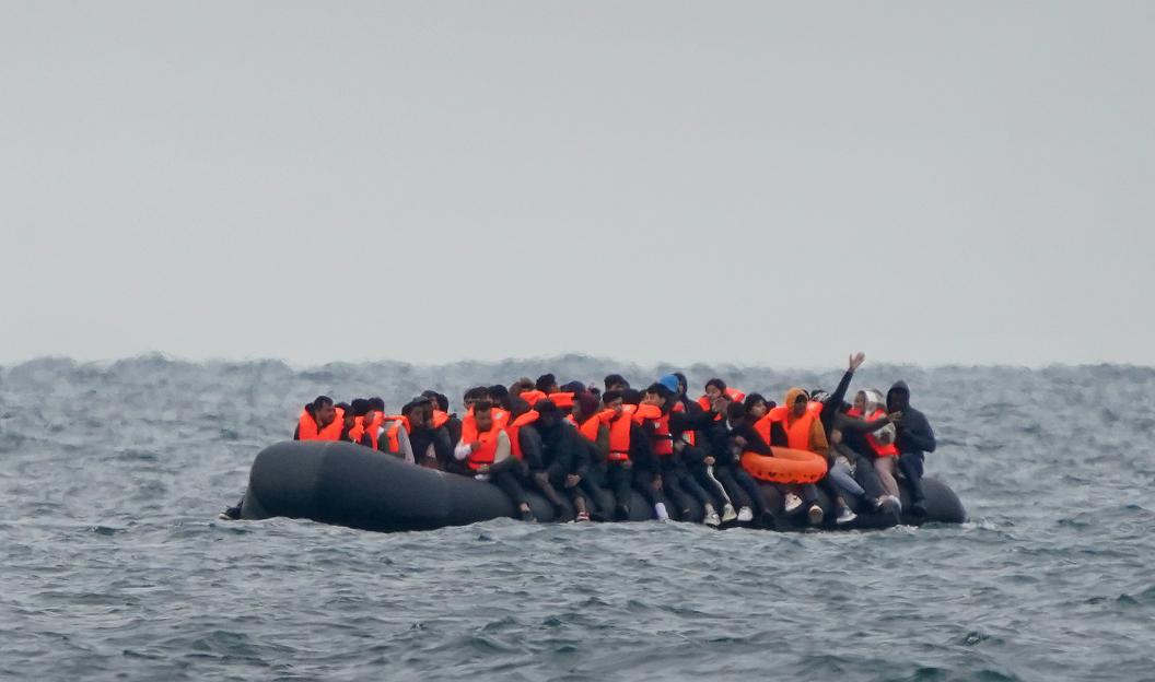 A group of migrants in a crowded inflatable boat with orange life vests crosses the Channel.
