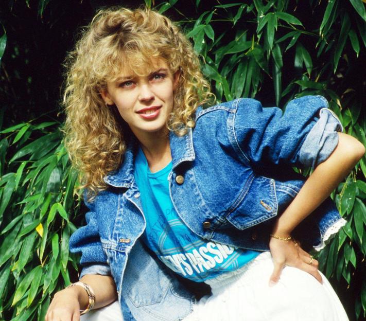 Kylie Minogue in a denim jacket and white pants in a promotional photo for the TV series "Neighbours".