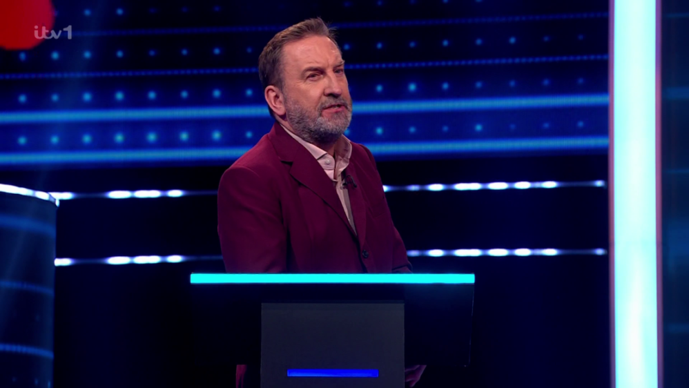 A man in a red jacket and light shirt standing behind a podium with a blue illuminated top.