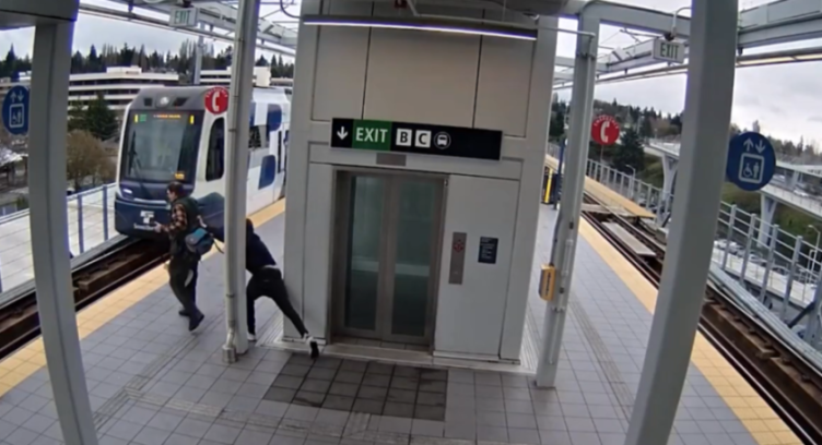 A man in a plaid shirt is shoved towards an oncoming train on a platform.
