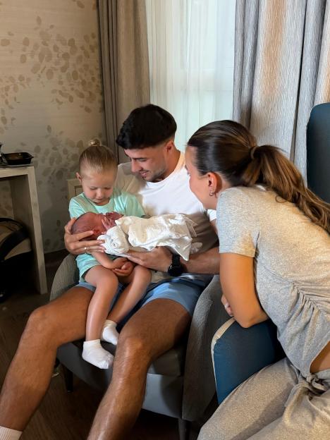 A man holds a baby while a little girl looks at the baby and a woman watches.