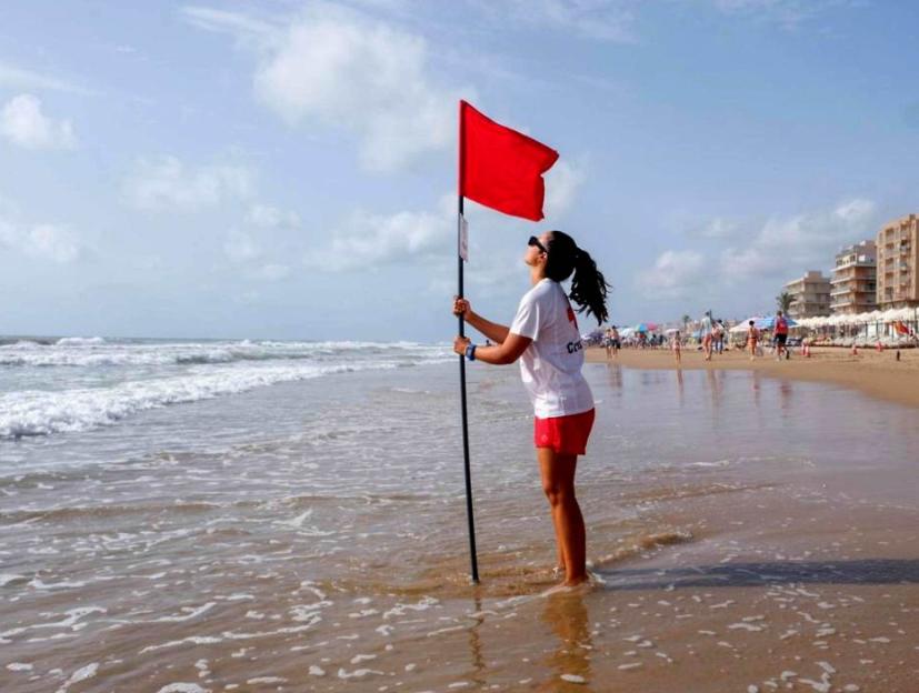 A lifeguard holding a red flag in the sea at a busy beach.