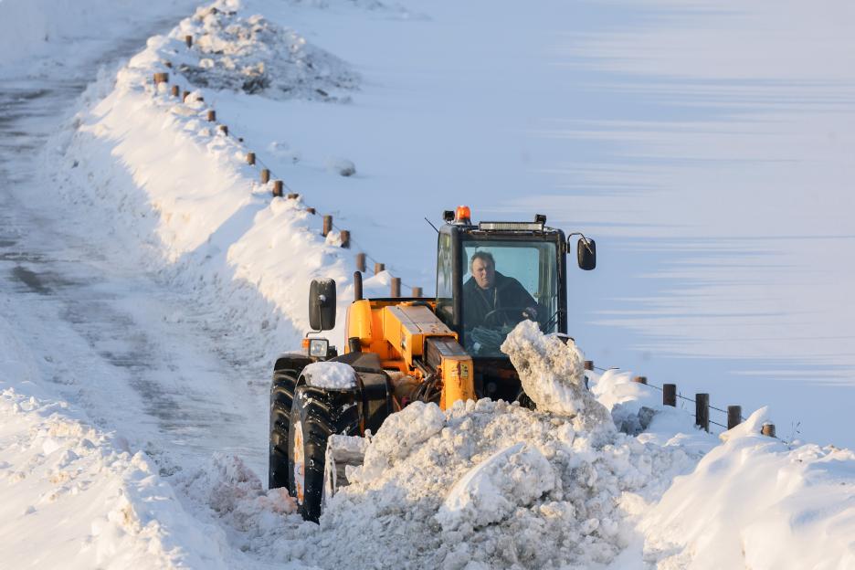 Man clearing snow from a road with a digger.