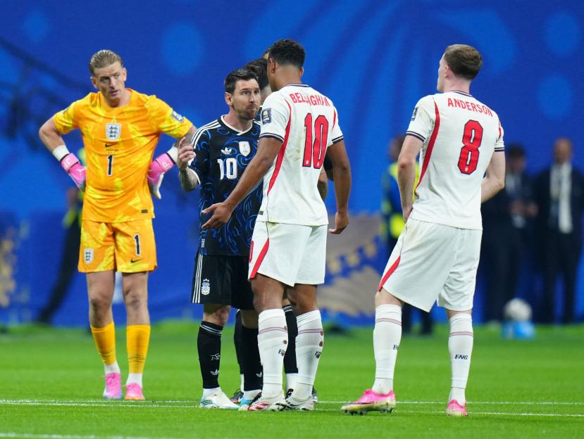 Argentina's Lionel Messi talking to England's Jude Bellingham and Harry Anderson on a soccer field.