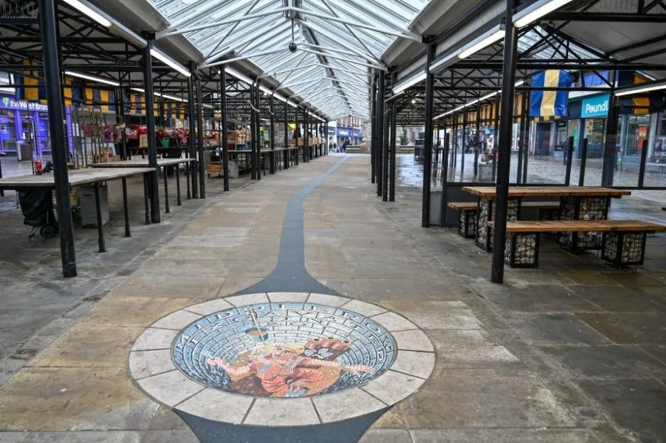 A nearly deserted covered market hall in Dudley, featuring empty stalls and a mosaic on the floor.